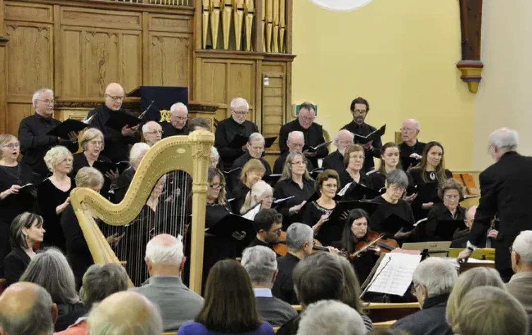 Group of singers in front of a pipe organ singing accompanied by a small stringed orchestra