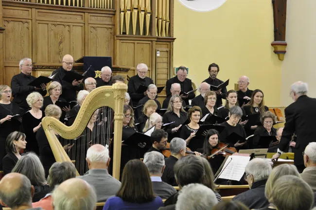 Group of singers in front of a pipe organ singing accompanied by a small stringed orchestra